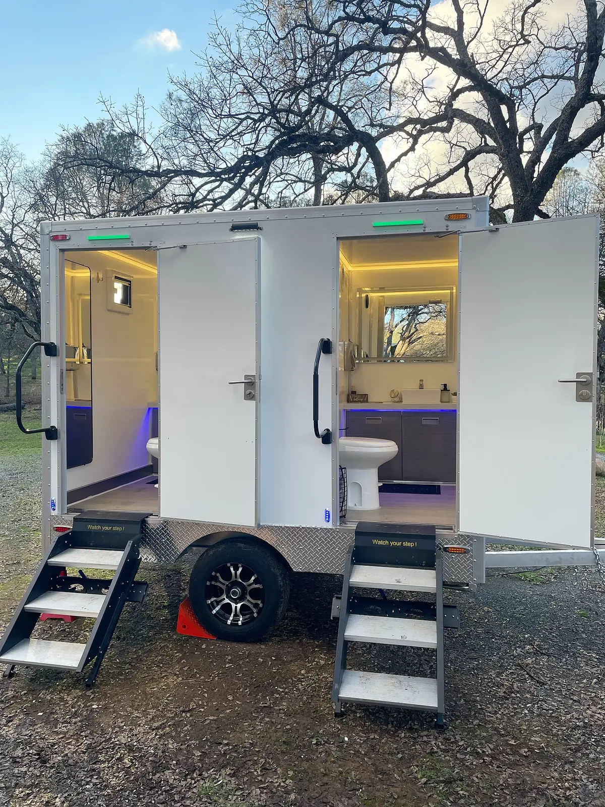 Two-stall restroom trailer with lit interiors at dusk during an evening event